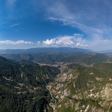 Uçsuz bucaksız dağ vadisi, dolambaçlı bir yol ve mavi gökyüzünün altında karla kaplı tepeler.