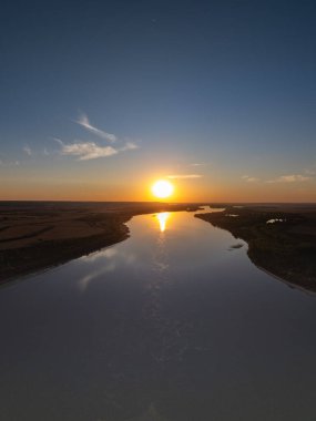 Geniş bir nehrin üzerinde altın gün batımı parlak güneşi ve engin mavi gökyüzünü yansıtıyor.