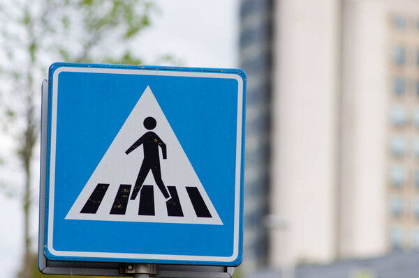 Blue pedestrian crossing sign with a building in the background in Arnhem, Netherlands