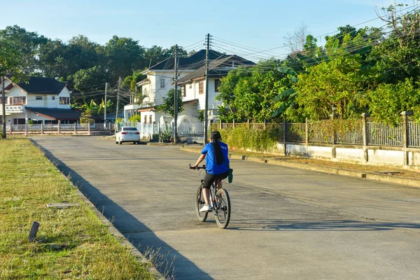 Rayong, Tayland 10 Ocak 2021 Kimliği belirlenemeyen kız sabah köy yolunda bisiklet sürüyor.