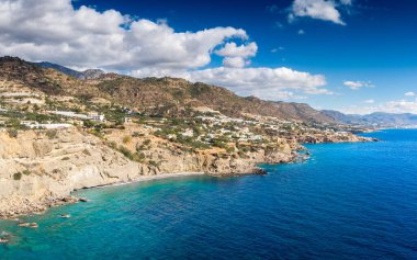 Gökyüzünde kabarık bulutlar olan kayalık dağ manzarasının yakınındaki cennet mavisi denizin manzarası