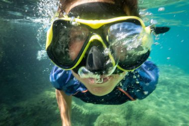 Suyun altında yüzen dalgıç maskeli bir çocuk.