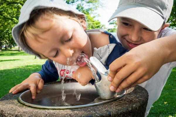 Sonriente Niño Ayudando Hermano Menor Beber Agua Pestaña Parque Público —  Fotos de Stock