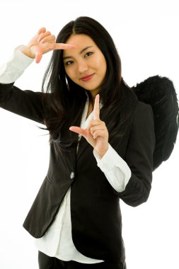 Siyah melek gibi giyinmiş Asyalı genç iş kadını beyaz arka planda izole edilmiş parmak çerçevesinden bakıyor.