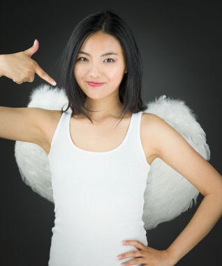 Asyalı genç kadın kendini kalça eliyle işaret eden bir melek gibi giyinmiş