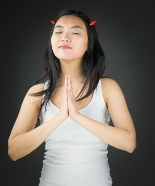 Asian young woman in devil horns in prayer position with hands clasped clipart