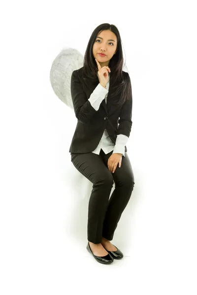Asiática joven empresaria sentada en taburete vestida como un ángel mirando hacia arriba con el dedo en la barbilla aislado sobre fondo blanco —  Fotos de Stock