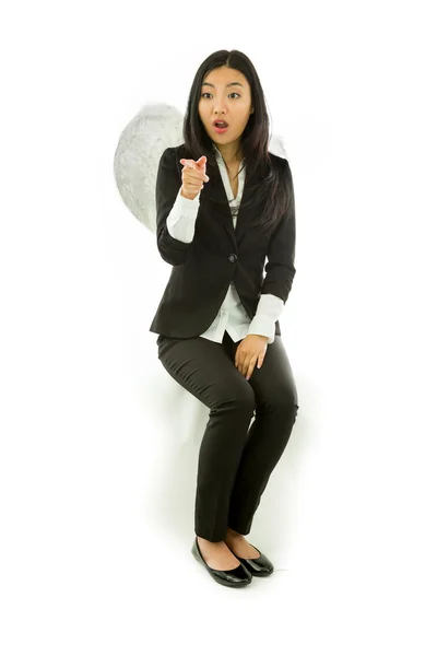 Schockierte asiatische junge Geschäftsfrau sitzt auf einem Schemel, der als Engel verkleidet ist und isoliert auf weißem Hintergrund zeigt — Stockfoto
