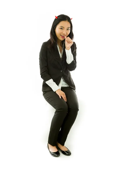 Asiática joven mujer de negocios sentado en taburete en el diablo cuernos pulgares en la boca aislado sobre fondo blanco —  Fotos de Stock