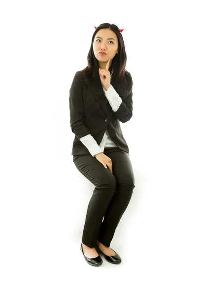 Asian young businesswoman sitting on stool in devil horns looking up with finger on chin isolated on white background — Stock fotografie