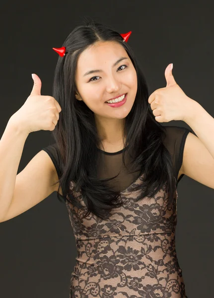 Asiático jovem mulher vestida como um diabo com mostrando polegar para cima sinal com ambas as mãos — Fotografia de Stock