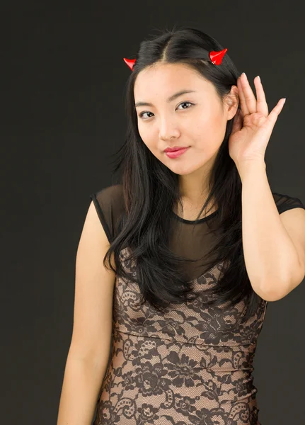 Asiatische junge Frau verkleidet als Teufel versucht, aufmerksam zuzuhören — Stockfoto