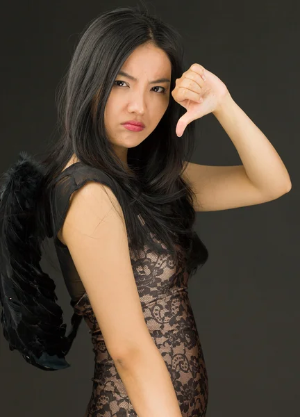 Upset Asian young woman dressed up as a black angel showing thumbs down sign — Stock Photo, Image