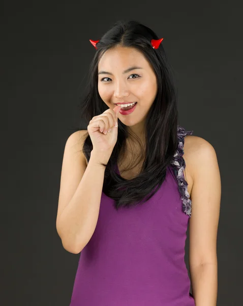 Teufelsseite einer jungen asiatischen Frau, die ihre Nägel beißt und lächelt — Stockfoto