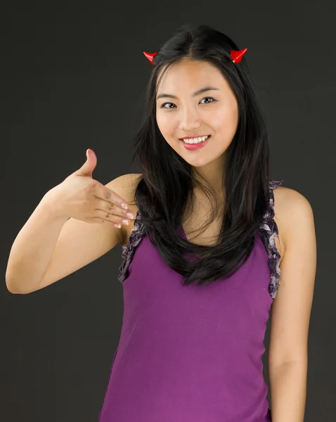 Teufelsseite einer jungen Asiatin, die lächelnd die Hand zum Händedruck reicht — Stockfoto