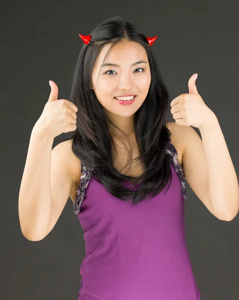 Lado diabólico de una joven asiática mostrando el pulgar hacia arriba con ambas manos y sonriendo — Foto de Stock