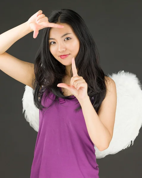 Ангельская сторона молодой азиатской женщины, делающей кадр пальцами и улыбающейся — стоковое фото