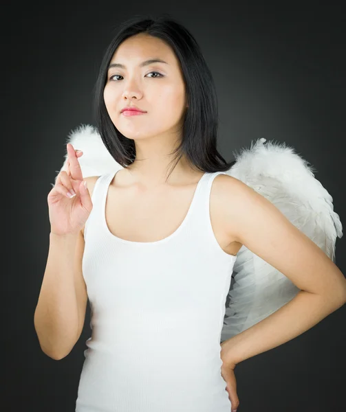 Азиатская молодая женщина, одетая как ангел, показывает свои пальцы, скрещенные рукой на бедре — стоковое фото