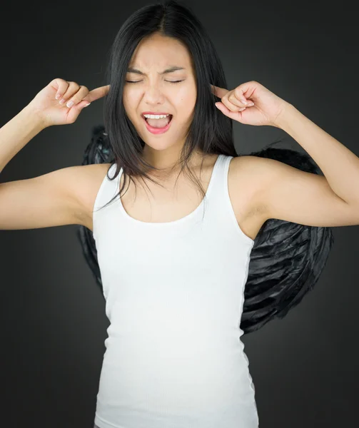 Asiática joven mujer vestida como un ángel gritando en frustración con los dedos en las orejas —  Fotos de Stock