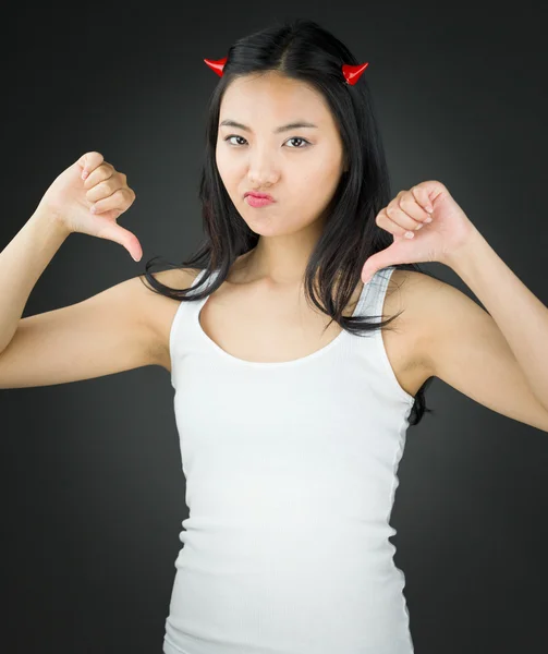 Junge asiatische Frau in Teufelshörnern aufgebracht und zeigt Daumen nach unten Zeichen aus beiden Händen — Stockfoto
