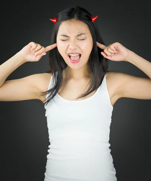 Aziatische jonge vrouw in duivel hoorns en schreeuwen in frustratie met vingers in de oren — Stockfoto