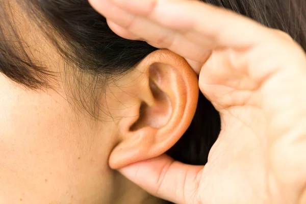 Extreme close-up of a young  woman with hands cupped on ear and trying to listen