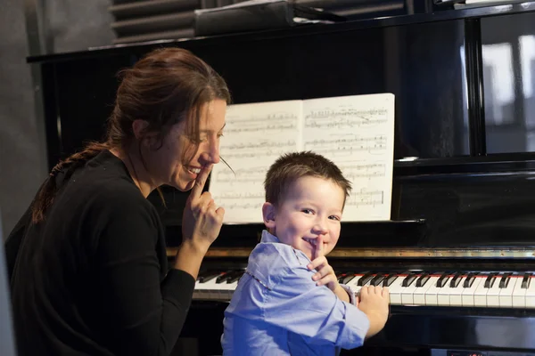 Ragazzo mettere indice dito sulle labbra con il suo istruttore di pianoforte e sorridente — Foto Stock