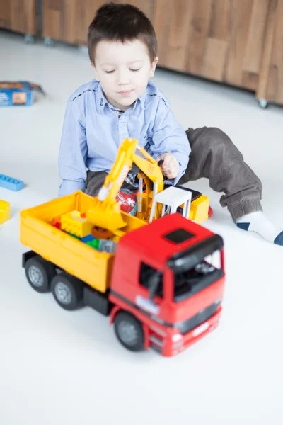 Rapaz bonito brincando com caminhões de brinquedo em casa — Fotografia de Stock