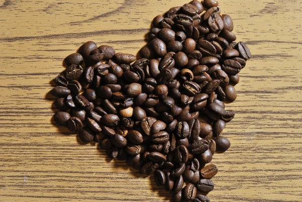 Photo of heart shaped heap of coffee beans on wood background — Stock Photo, Image