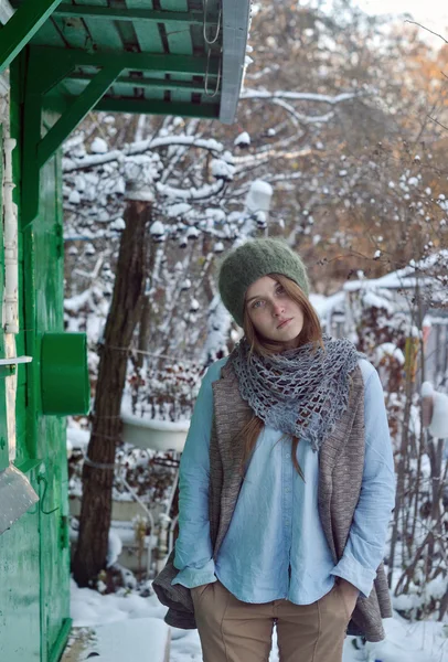 Retrato de inverno de bela menina triste vestindo chapéu verde e casaco de pé perto da casa verde — Fotografia de Stock