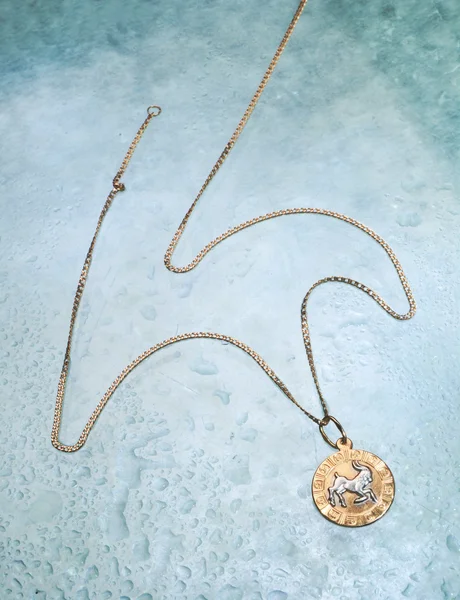Bellissimo medaglione d'oro e catena su sfondo blu goccia d'acqua — Foto Stock