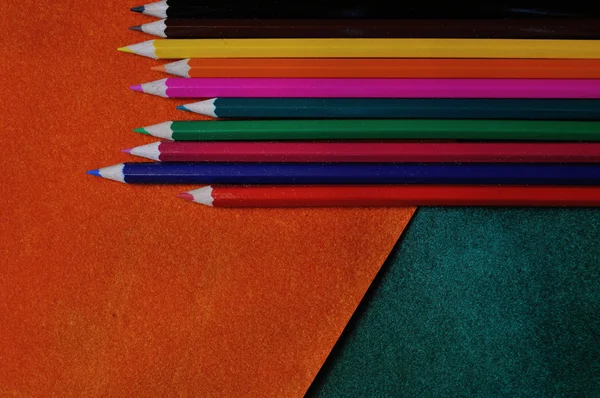 Multicolored pencils on orange and green abstract textured background