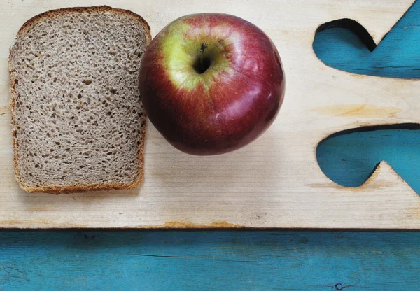 Piece of bread and apple on cutting board and blue background