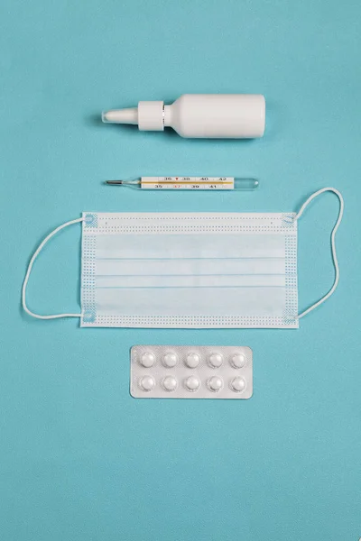 Medical thermometer, medicine mask, drops and pills on blue background. Top view of doctor workplace. Flat lay composition.