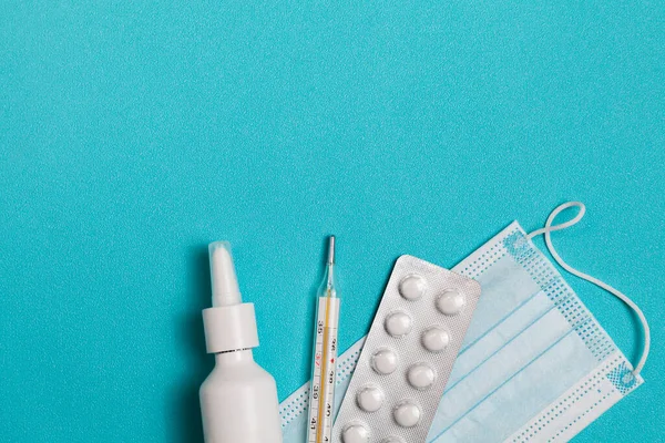 Medical thermometer, medicine mask, drops and pills on blue background. Top view of doctor workplace. Flat lay composition.