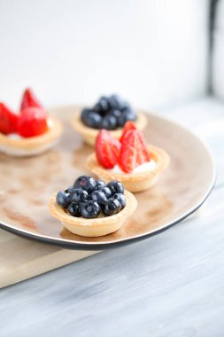 Peynir kremalı kek ve taze çilek ve ahşap arka planda bej bir tabakta yabani böğürtlen. Yemek tarifleri ve tatlılar için bir fikir. Mükemmel parti bireysel taze meyve tatlısı..