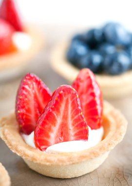 Peynir kremalı kek, taze çilek ve arka planda bej bir tabakta yabani böğürtlen. Yemek tarifleri ve tatlılar için bir fikir. Mükemmel parti bireysel taze meyve tatlısı..