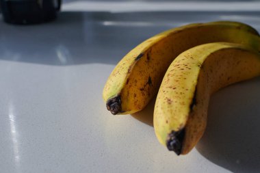 Güneşli bir günde beyaz mutfakta siyah benekli iki sarı muz olgunlaşıyor.
