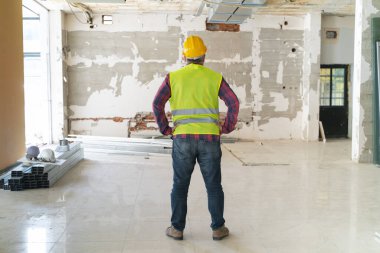 İnşaat alanında çalışan, koruyucu kasklı, inşaat aletleriyle ayakta duran bir inşaat işçisi.