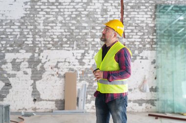 Bir atölyede kahve molası sırasında planları analiz eden inşaat işçisi.