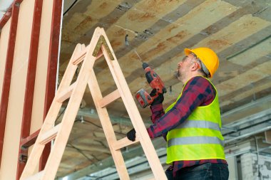 Bir merdivende tamirci elinde bir makineyle tavana sondaj yapıyor.