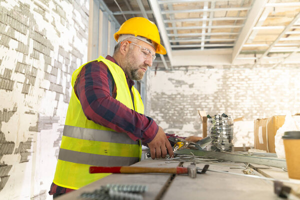 Builder in working uniform with protective helmet standing with instruments at the construction site indoors