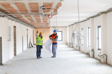 Güvenlik yelekleri giyen iki adam bina inşaatında tartışıyorlar.