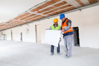 İnşaat işçileri inşaat alanının planlarına bakıyor..