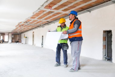 İnşaat alanında dururken mimari planı kontrol eden iki mimar 