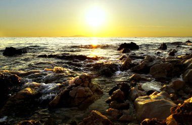 Taş plajın üzerinde parlak ve ışıl ışıl deniz batışı ve kayaların arasında dalgalanan sığ su. Hırvatistan 'ın Güzelliği