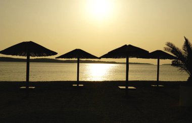 Güneş şemsiyeleri güneş batımında ve altın saatinde deniz kenarında tatil köyünde.