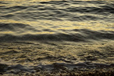 Pebbles in the shallow sea water and foamy waves that hitting the coast