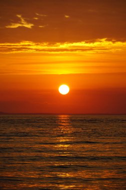 Gün batımının yoğun ve canlı kırmızı-turuncu renkleri yavaşça akan denizin üzerinde