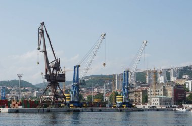 Rijeka, Hırvatistan, 6 Haziran 2025. Büyük liman turnaları sakin deniz suyunun üzerinde yükselir, yumuşak akşam renklerini yansıtır, endüstriyel yapı ve doğal güzellikleri birleştiren huzurlu bir kıyı manzarası, seyahat ve mimari kavramlar için idealdir.